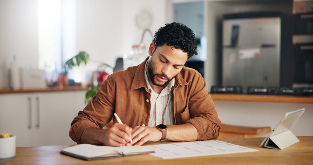 Man aan keukentafel controleert documenten en maakt notities voor leningaanvraag