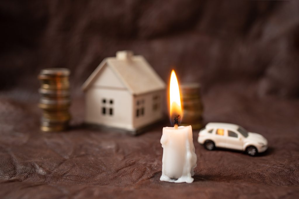 Brandende kaars met miniatuurhuis, auto en munten als symbool voor lening bij overlijden en financiële bescherming.