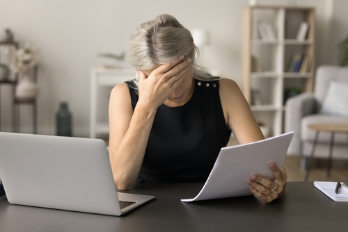 Bezorgde vrouw bekijkt financiële documenten naast haar laptop