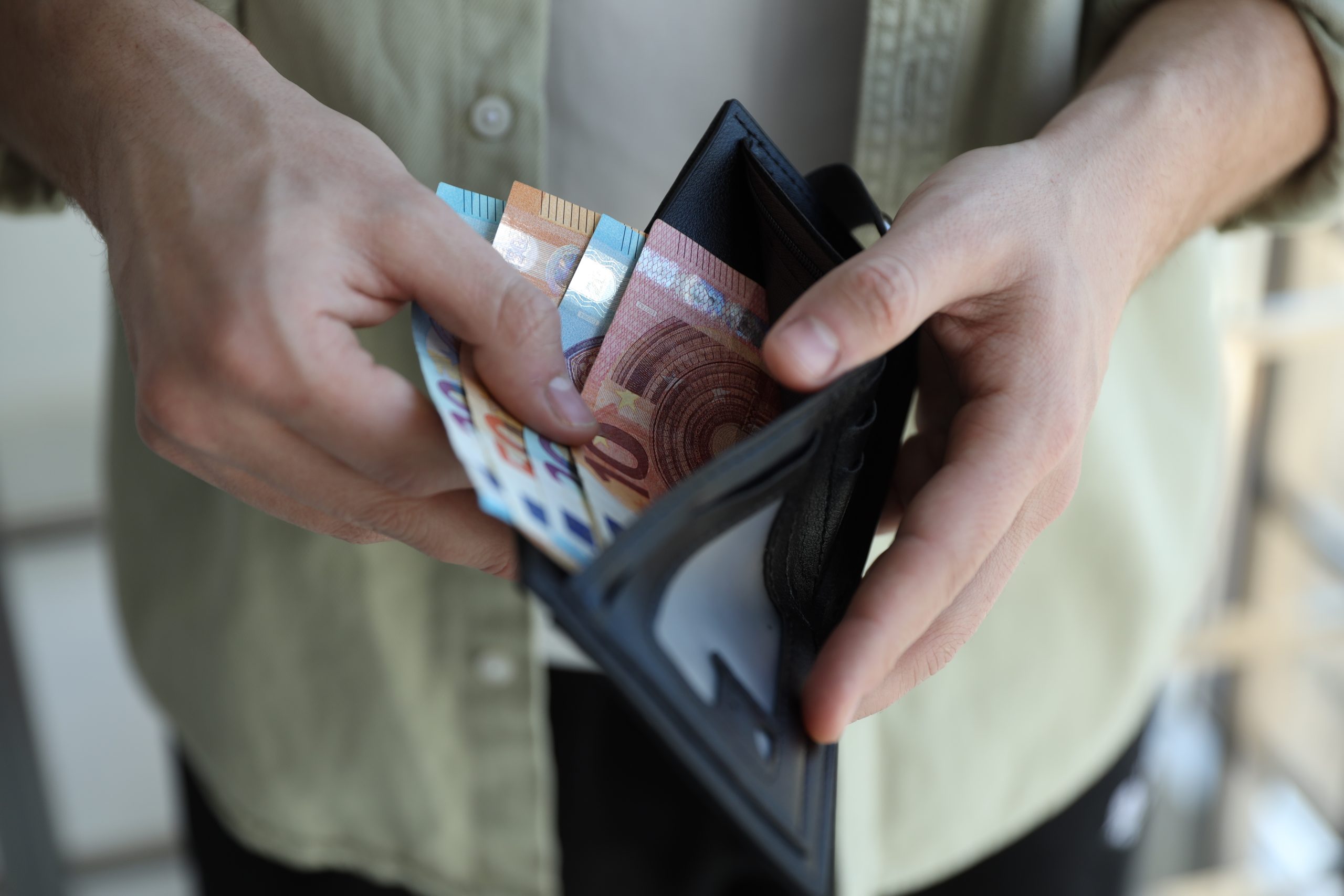 Handen halen eurobiljetten uit een zwarte portemonnee